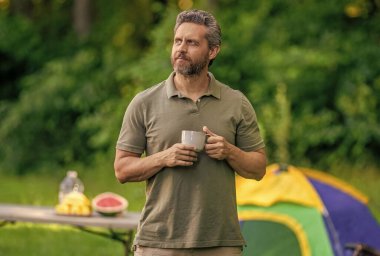 Kamp macerası. Yürüyüş konsepti. Kamp çadırı. Kahve fincanı. Adam ormanda sabah kampı kahvesi içiyor. Yaz günü doğa yürüyüşçüsü. Yaz kampı ve doğa tatili. Yaz kampındaki adam..