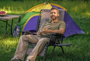 Kamp çadırı. Kahve fincanı. Ormanda sabah kahvesi içen bir adam. Yaz günü doğa yürüyüşçüsü. Yaz kampı ve doğa tatili. Yaz kampındaki adam. Kamp macerası. Yürüyüş kavramı.