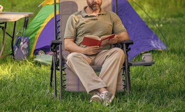 Kitap okuyorum. Adam ormanda kampta kitap okuyor. Yaz günü doğa yürüyüşü. Yaz kampı ve doğa tatili. Yaz kampındaki adam. Kamp macerası. Yürüyüş inzivası. Kesik manzara. Kamp çadırı.