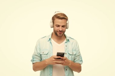 Kulaklıklı adam telefonda mp3 çalma listesini seçiyor. Beyazlar içinde izole edilmiş akıllı telefon uygulaması kullanan adam. Telefonla müzik dinlemek. Müzik yaşam tarzı. Ses çalma listesi. Kulaklıklı adam. Günlük tutma.