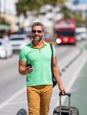 Turist tatili rezervasyonu. Yaz gezisi için seyahat valizi. Yaz gezisini ayarlayan adam. İspanyol turist gezginleri kitabı internette. Seyahat çantalı bir turist. Gezgin telefon kullanıyor. Otobüs durağı.