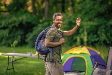 Ormanda çadırlı sırt çantalı bir adam. Yaz günü doğa yürüyüşçüsü. Yaz kampı ve doğa tatili. Yaz kampındaki adam. Kamp macerası. Yürüyüş konsepti. Kamp çadırı. Merhaba..