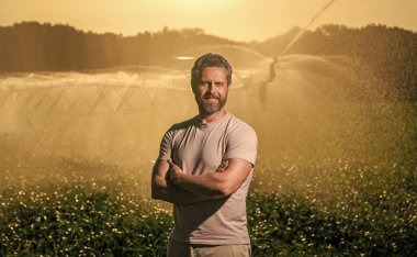 Damlatma sulama sistemi. Gün batımında mahsul sulama. Tarım ve tarım. Sulama sisteminde tarımı sulayan bir adam. Kırsal kesimde bir çiftçi. Su fıskiyesi sulama tarlası.