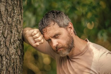 Hispanik olgun ve vahşi sakallı bir adam ormanda ağaçlara yaslandıktan sonra yorgun ve terliyor..
