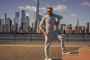 New York 'ta sporcu. Manhattan 'da spor kıyafetli bir adam. Vücuduna uygun. Yoga koçu. Sporcu adam antrenmana hazır. Sağlıklı bir yaşam tarzı. Spor ve spor. Eğitim için yoga minderi. Güneşli bir gün.