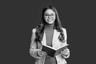 Gözlüklü liseli kız, 1 Eylül 'de kırmızı üzerine izole bir şekilde sonbahar ceketi giyerek bilgi ve eğitim kitabı okuyor..