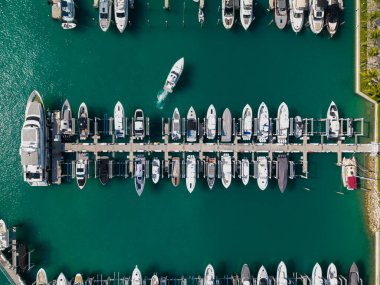 Marinaya yanaşmış lüks yatların havadan görüntüsü. Yatların yukarıdan aşağıya insansız hava aracı görüntüsü. Tekneler ve yelkenliler manzaralı deniz kıyısında. Yat kıyı şeridi boyunca ilerliyor. Şafak vakti liman gemilerle doldu.