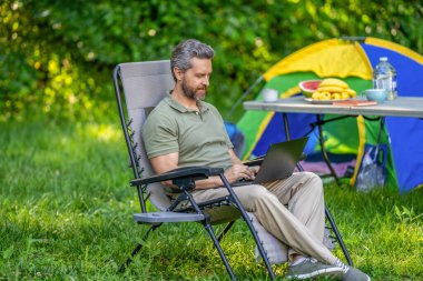 Kamp alanı yönetimi. Kampta dizüstü bilgisayarda daktilo yazan bir iş adamı. İnternette çalışan bir iş adamı. Serbest çalışan bir iş adamı. Dışarıda çalışan bir iş adamı. Ormanda çadırda piknik yapan bir adam..