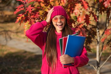 Sonbahar ders çalışma zamanıdır. Eğitim ve bilgi. Okul eğitimi. Okula dönüyorum. Sonbahar kızı okul ödevini tutuyor. Üniversite öğrencileri için eğitim. Sonbaharda açık havada genç bir kız. Ömür boyu öğrenme.
