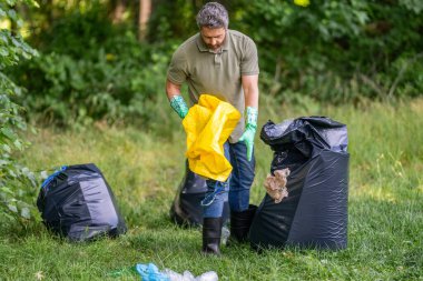 Environmental activist. Environmental conservation and waste pollution. Environment plastic pollution. Volunteer collecting trash into garbage bag. Environmental protection. Plastic waste cleanup.