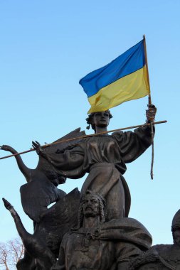 Mavi gökyüzünün arka planında Ukrayna bayrağını tutan bir kadının bronz heykeli. Özgürlük mücadelesi. Rusya 'nın Ukrayna' ya saldırması. Rus-Ukrayna savaşı.