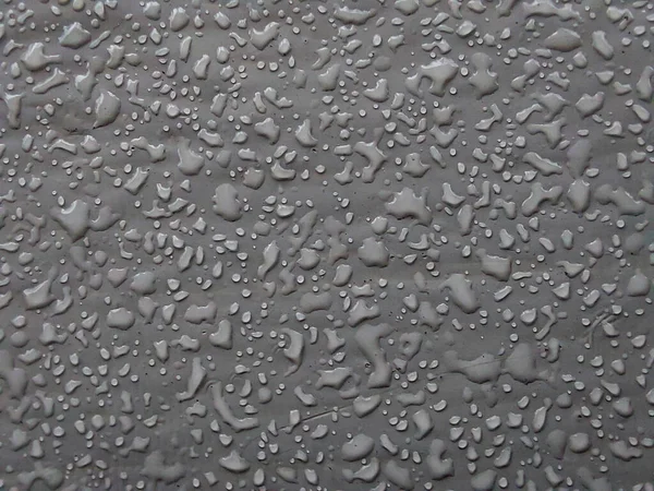 灰色の表面に雨が降った後の水の滴 マクロ写真 水のドロップフィールドの浅い深さでクローズアップ撮影した 背景画像 — ストック写真