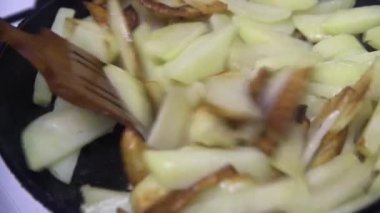  Tahta kaşık patatesleri kızartma tavasında karıştırıyor..