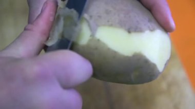 Büyük bir patatesi bıçakla soyan eller..