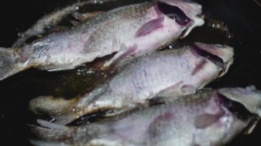 Tahta kaşıkla bir el, tavadaki balığı kontrol eder.