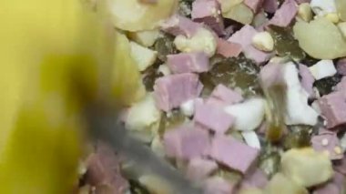 a spoon stirs a salad of sausage potatoes and pickled cucumbers, close-up.