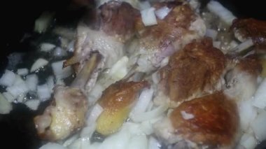 a spoon stirs the chopped onion with chicken drumsticks with an appetizing crust, close-up.