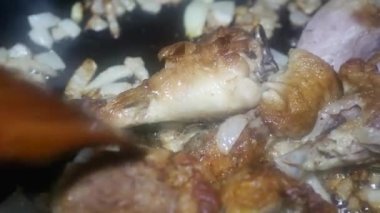 a wooden spoon stirs chicken drumsticks with an appetizing crust and onions in a frying pan, macro