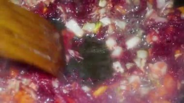 a spoon mixes chopped carrots, onions and beets for borscht in a pan