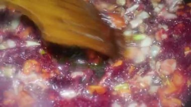 a spoon adds a paste of red vegetable peppers to a pan with chopped carrots, onions and beets for borscht.