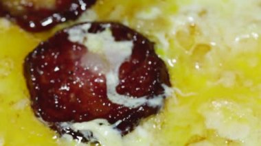 macro video of omelette and sliced sausage with crust and onion frying in a frying pan.