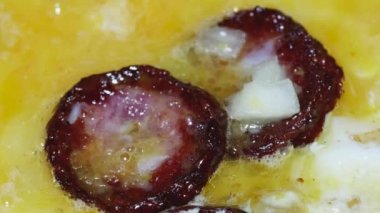 macro video of scrambled eggs and sliced sausage with crust and onion frying in a frying pan.