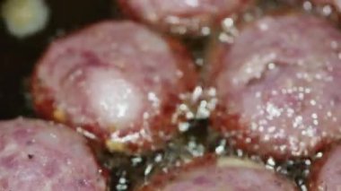 macro video of sliced sausages frying in boiling oil in a frying pan.