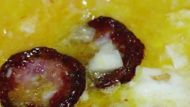 omelet from eggs and sliced fried sausage with onions in a frying pan, close-up.