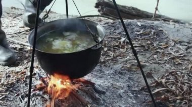  Nehir kıyısında bir kazanda balık çorbası pişirmek, bir kaşıkla balık çorbasını karıştırmak.