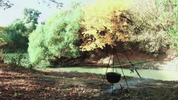 釣りのための回転棒の近くの薪の上のカルドロン 美しい川の岸で魚のスープを調理する — ストック動画