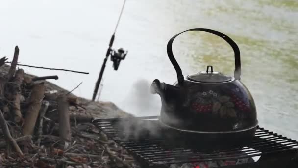 在燃烧的灰烬之上沸腾的茶壶 在河流的背景下 — 图库视频影像