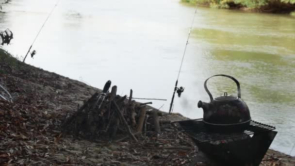 石炭をめぐるティーポット 釣り棒と川の背景に対して — ストック動画