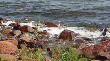 Denizin dalgaları kumsaldaki kahverengi taşlara ağır çekimde çarptı..