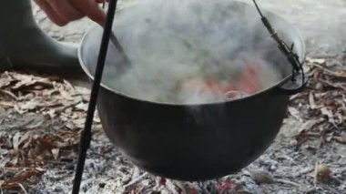  Balık çorbasını kepçeyle karıştırmak, kazanda balık çorbası pişirmek doğadaki bir ateşin üstünde.