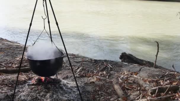 川の近くの自然の中の火でカルドロンで魚のスープを調理する — ストック動画