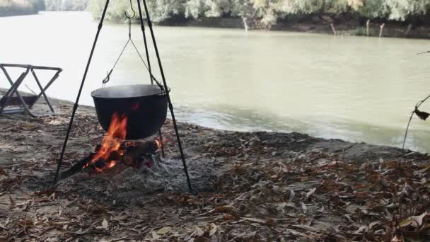 食糧をカルドロンの火の上に 速い川の岸で調理する — ストック動画
