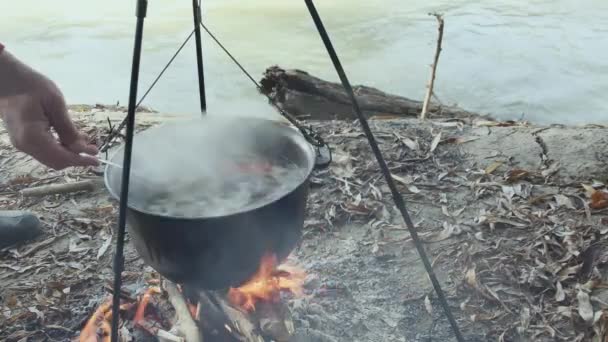 カルドロンのスプーンで魚のスープをかき混ぜ 自然の火でカルドロンで魚のスープを調理する — ストック動画
