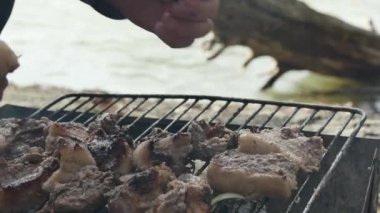 Bir adam nehir kıyısında, elleri ile bir parça sıcak domuz boynunu devirir..