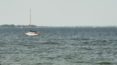  Dalgalar bir yerde sallanıyor, bir yelkenli de geçen ördeklerin yanında, ağır çekimde.