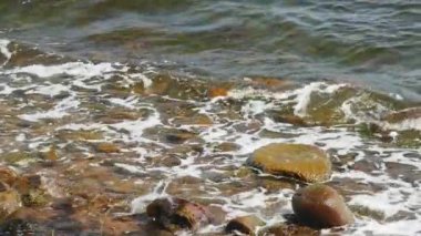 Küçük deniz dalgaları yavaş çekimde kahverengi taşlara çarpıyor.