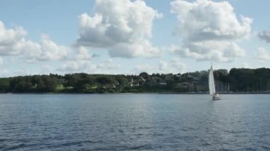 Sahilde ağaçlar ve kumsal olan bir kıyıya karşı yelken açmış yüzen bir yatın manzarası..