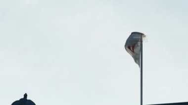 Rüzgarda dalgalanan beyaz bayrak ve gökyüzünde kırmızı bir Malta haçı