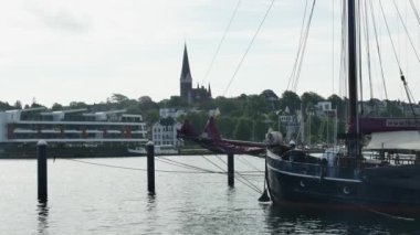  Flensburg, Almanya - 27 Temmuz 2023. Kilisenin önünde kırmızı yelkenli demirli bir yelkenli.