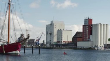  Flensburg, Almanya - 27 Temmuz 2023. Limanı gören binalar, demirli yatlar, kanoyla denize açılan bir adam ve Ryvar 'ın 1916' da inşa ettiği balıkçı teknesi.