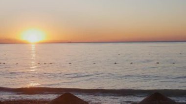  Beautiful morning scene on a tropical or Mediterranean beach. The large, bright sun creates a lens flare and glittering reflection on the water.