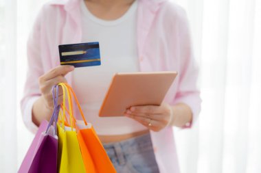 Elinde kağıt torba tutarken dijital tablet alışverişi yapan Asyalı genç kadının elleri, alım-satım, ödeme, iş konsepti ile ödeme yapan kadınların elleri.