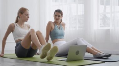 Two young people woman practicing exercise or yoga on mat while watching laptop computer tutorial online at home, woman having motivation looking notebook for workout, lifestyles and sport concept.