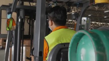 Genç Asyalı adam forklift kutusu kullanıyor ya da fabrikadaki depodaki konteynırlarda nakliye ve dağıtım için ambalaj yapıyor, depoda çalışan, lojistik ve nakliye konseptinde çalışan.