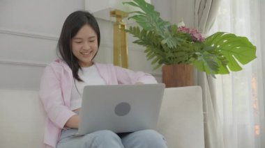 Happiness young asian woman sitting on sofa and working on laptop computer while successful and excitement at home, freelance female using notebook and achievement, business and lifestyles concept.