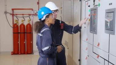 Electrical young woman and man engineer examining maintenance cabinet system electric in the control room at industrial factory, technician or electrician inspection power distribution.